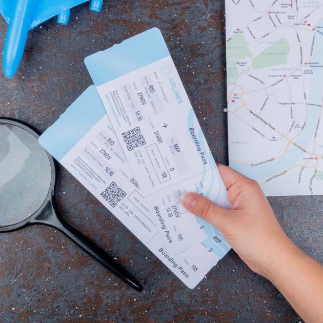 top view of female hands holding plane tickets with magnifying glass on a black background